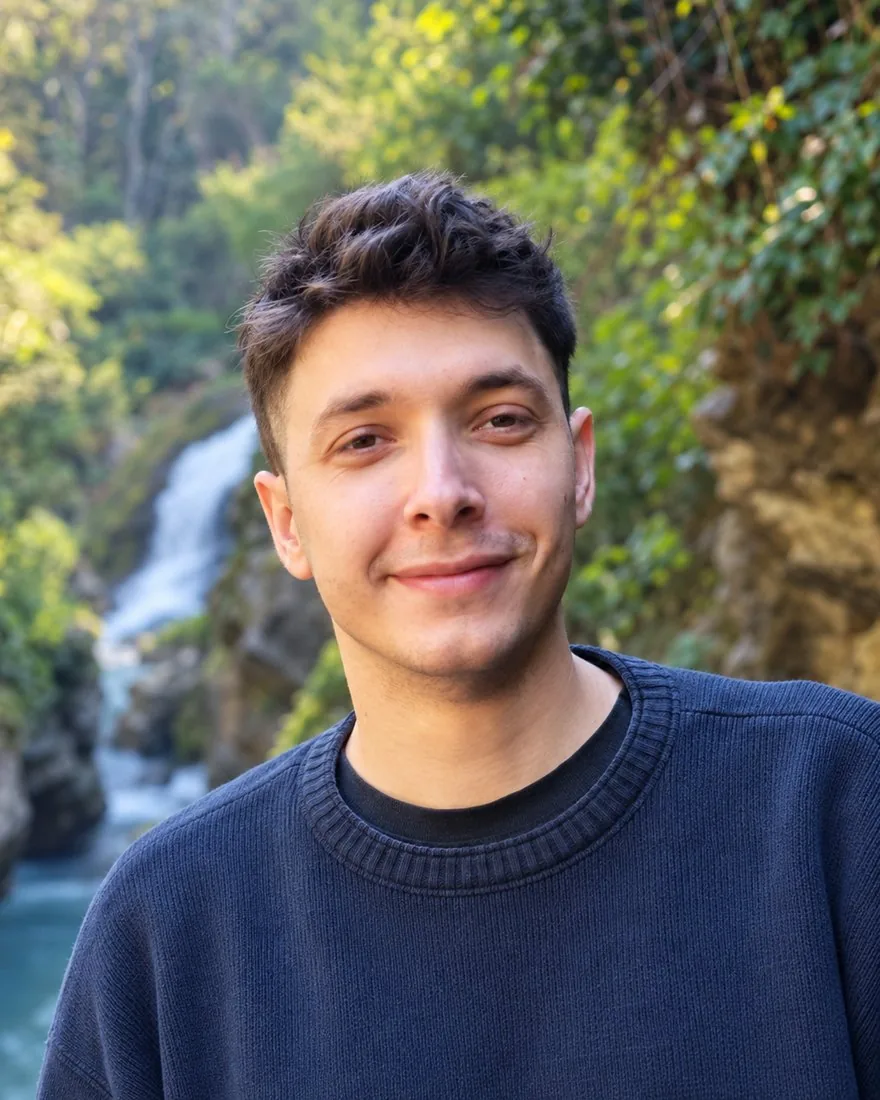 Manuel Di Chiara sorridente, con un maglione blu, davanti a una cascata